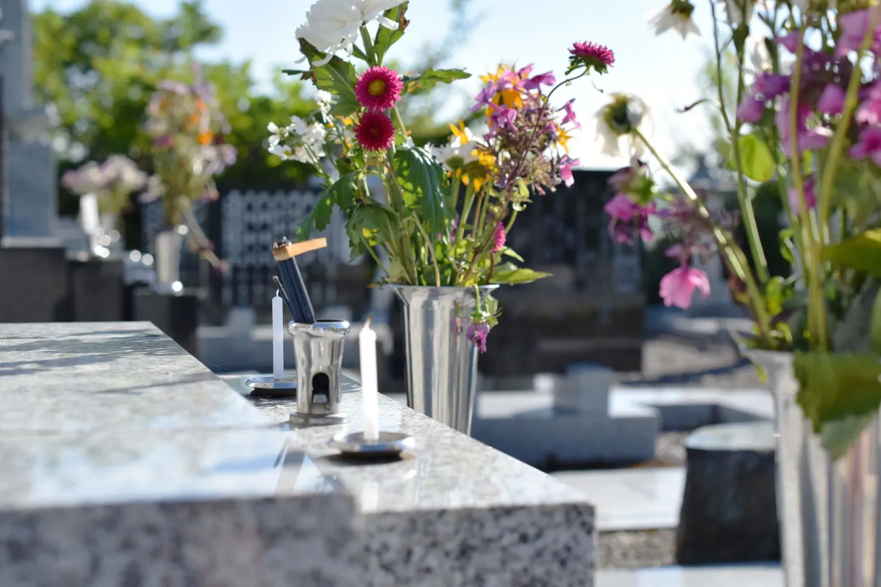 Vase de fleurs et bougies allumées sur une pierre tombale au cimetière.